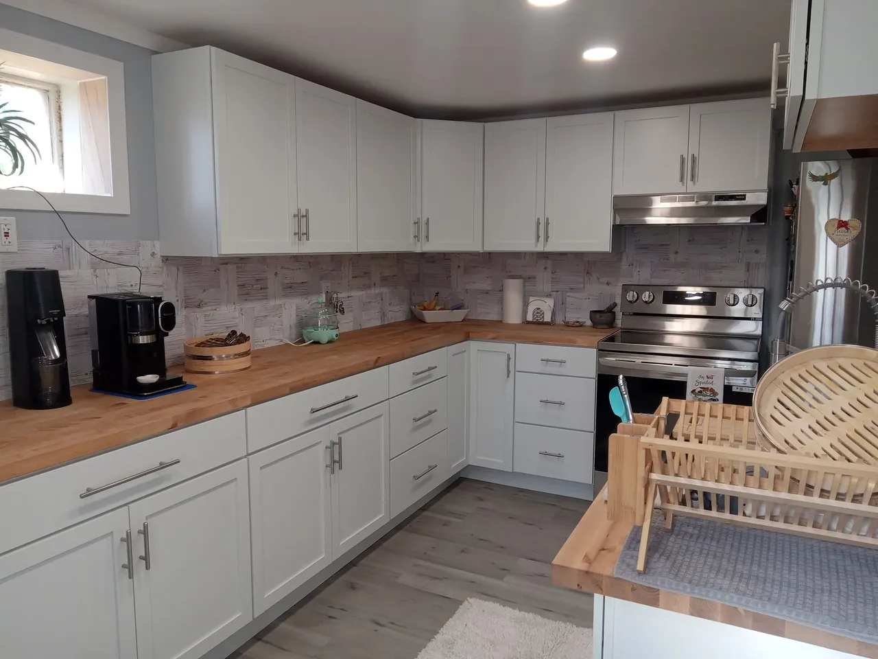 White kitchen cabinets with wood counters, tile backsplash, and stainless appliances